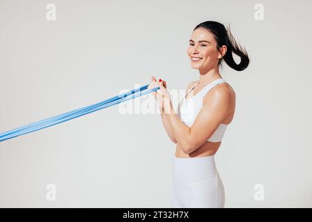 Vista laterale di una giovane atleta sorridente che si piega le mani utilizzando una fascia di resistenza Foto Stock