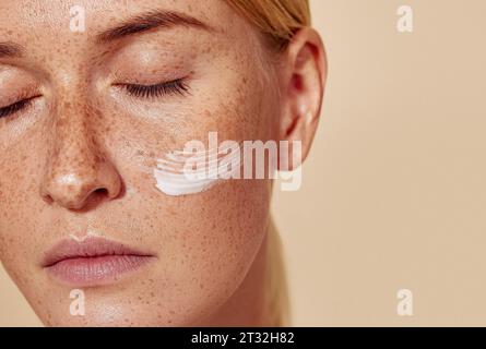 Ripresa ravvicinata e dettagliata di una giovane donna con idratante sulla guancia Foto Stock