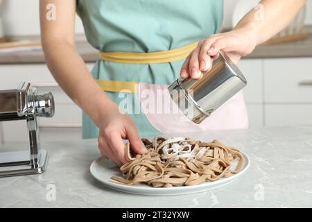 Donna spruzzando soba crudo (tagliatelle di grano saraceno) con farina al tavolo grigio in cucina, primo piano Foto Stock