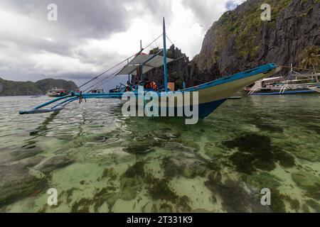 Tradizionali battelli filippini banca con balenieri ancorati nella remota baia tropicale nascosta con scogliere rocciose frastagliate Foto Stock