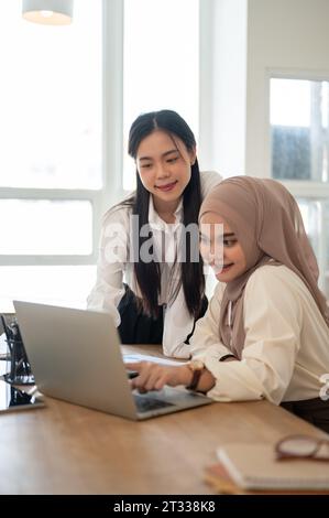 Una bella e professionale donna d'affari asiatica-musulmana che usa il suo computer portatile mentre discute di lavoro con un collega nella sala riunioni. Foto Stock