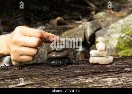 Un primo piano della mano di una donna che mette una piccola pietra su un cumulo di roccia per fare un cairn nel nord dell'Idaho. Foto Stock