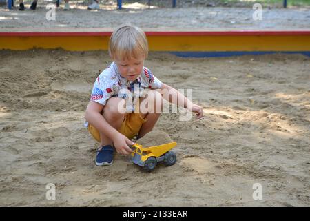 Simpatico bambino che gioca sulla sabbia nel parco giochi all'aperto. Un bel bambino che si diverte nelle calde giornate estive. Foto di alta qualità Foto Stock