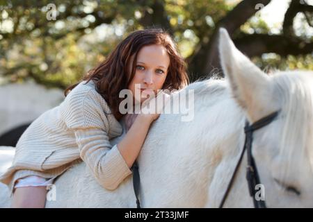 Natura, ritratto e donna che poggia sul suo cavallo in una fattoria all'aperto per le corse sportive. Sorridi, felice e giovane dal Canada con il suo equestre Foto Stock