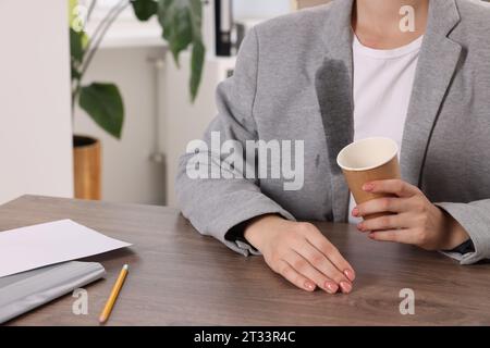 Donna che mostra macchie di caffè sulla giacca al tavolo di legno all'interno, primo piano Foto Stock