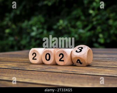 Felice anno nuovo 2024 con inizio di nuove storie, tendenze e business. Concetti di sostenibilità ambientale. Capovolgere da 2023 a 2024 numeri su un cubo eco in legno Foto Stock