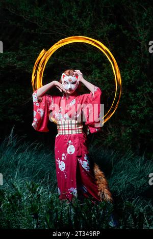 ragazza in maschera con coda di volpe in un cerchio di fuoco Foto Stock