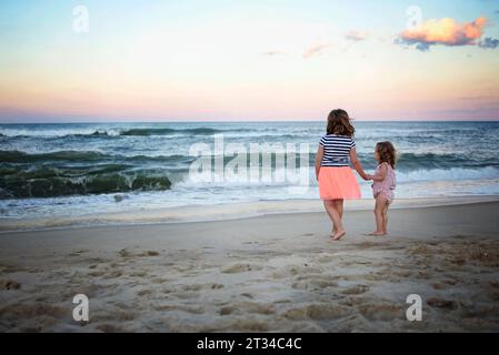 Sorelle che si tengono per mano guardando il tramonto sull'oceano Foto Stock