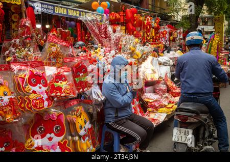 Una donna vietnamita che vende regali colorati rossi e dorati per Tet, o Capodanno lunare, guarda il suo cellulare a Hang ma, Hanoi, Vietna Foto Stock