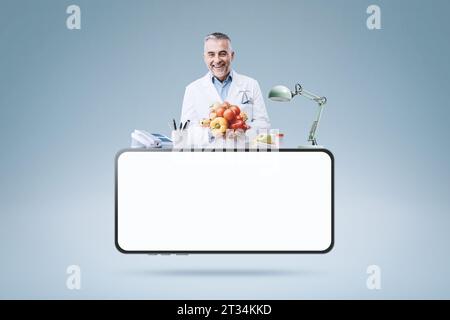 Nutrizionista professionista che lavora nel suo ufficio e smartphone con schermo vuoto: telemedicina e concetto medico online Foto Stock