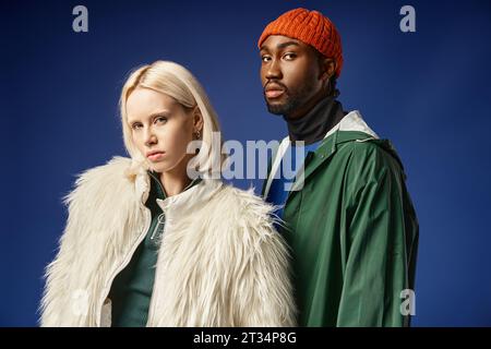 donna bionda in posa con un uomo afro-americano in abbigliamento invernale, modelli alla moda su sfondo blu Foto Stock