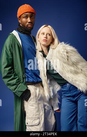 coppia interrazziale in posa su sfondo blu, donna con giacca in pelliccia sintetica e uomo afro-americano Foto Stock