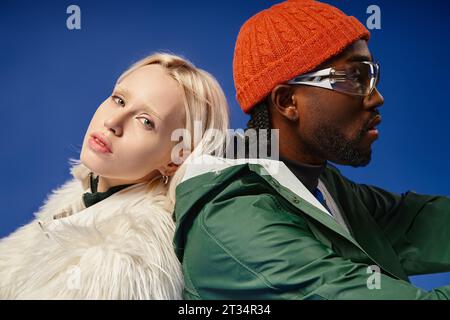 modelli multiculturali con outfit invernali alla moda che si presentano insieme su sfondo blu, diversità e stile Foto Stock