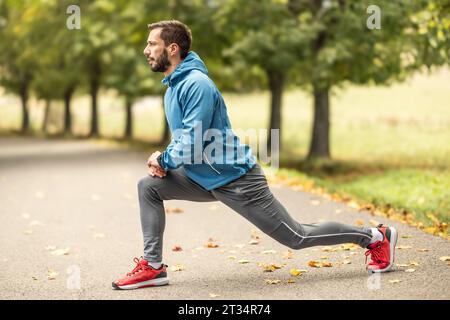 Un giovane atleta si sta riscaldando prima di allenarsi nel parco. Riscalda la parte inferiore del corpo. Foto Stock