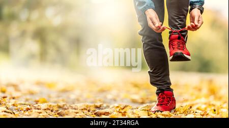 Una vista ravvicinata delle mani di un atleta che si lega i lacci delle scarpe prima di correre in un parco autunnale. Foto Stock