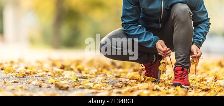 Una vista ravvicinata delle mani di un atleta che si lega i lacci delle scarpe prima di correre in un parco autunnale. Foto Stock