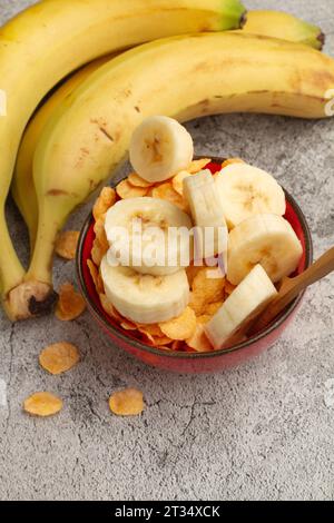Una mano di banane e cereali per la colazione con fette di banana in una ciotola su un bancone da cucina in marmo Foto Stock