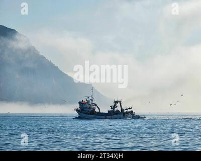 Una piccola barca da pesca è vista alla deriva nell'oceano aperto in una giornata nebbiosa Foto Stock