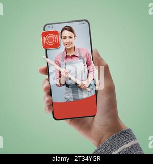 Cuoca donna con una biforcetta sullo smartphone: Noleggia professionisti online Foto Stock