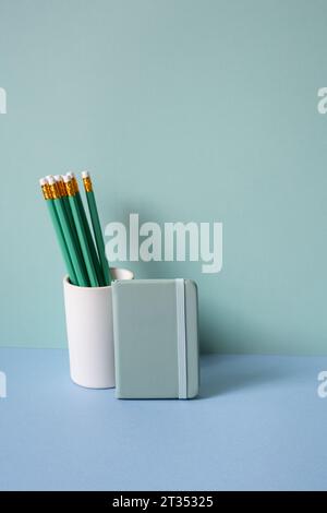 Portamatite e diario su scrivania blu. sfondo verde menta Foto Stock