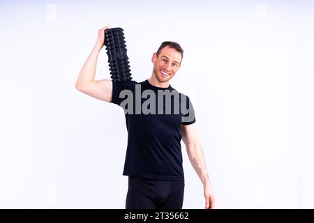 Athletic uomo usando un rullo in gomma spugna per alleviare muscoli doloranti dopo un allenamento. Foto Stock
