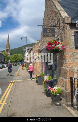 Ballater Village Royal Deeside, affacciato a nord su Bridge Street, nel centro del villaggio. bellissimi cestini sospesi. Negozi e turisti. Ballater villag Foto Stock