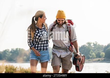 Felice coppia giovane con zaini e chitarra a piedi lungo il fiume Foto Stock