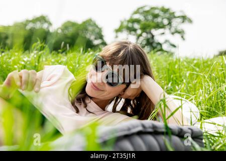 Rilassata donna sdraiata su un prato a leggere un libro Foto Stock