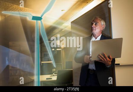 Immagine digitale composita di un uomo d'affari che guarda alla futuristica turbina eolica in ufficio Foto Stock