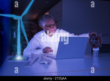 Uomo d'affari con un computer portatile che esamina la macchina alla scrivania Foto Stock