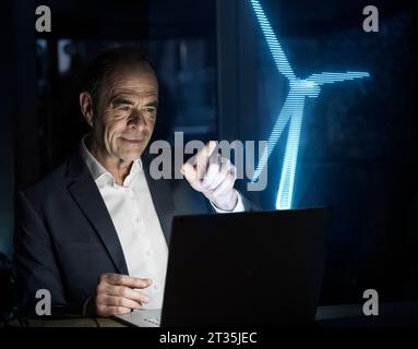 Uomo d'affari che punta alla futuristica turbina eolica in ufficio Foto Stock