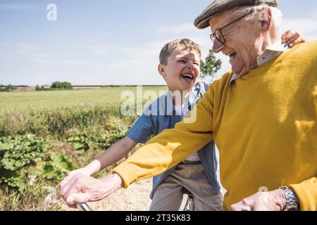 Happy boy seduto in bicicletta e divertito con il nonno nella giornata di sole Foto Stock