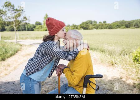 Ragazza che indossa un cappello a maglia che bacia nonno sulla fronte Foto Stock