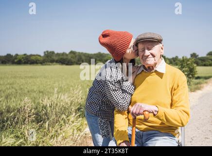 Ragazza che indossa un cappello a maglia che baciava il nonno nelle giornate di sole Foto Stock