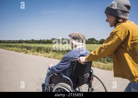 Ragazza felice che spinge la sedia a rotelle con il nonno nelle giornate di sole Foto Stock