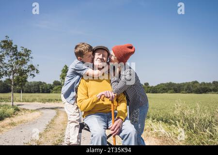 Ragazzo e ragazza che baciano nonno in un giorno di sole Foto Stock