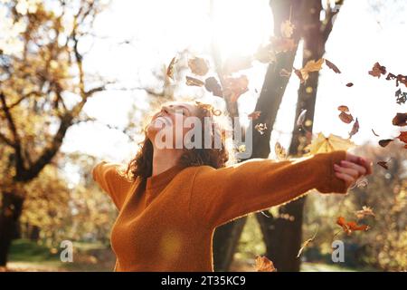 Donna rossa con le braccia allungate che si gode le foglie autunnali che cadono al parco Foto Stock