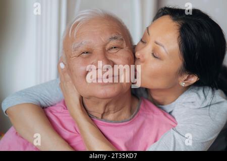 Figlia adulta che bacia padre anziano sulla guancia a casa Foto Stock