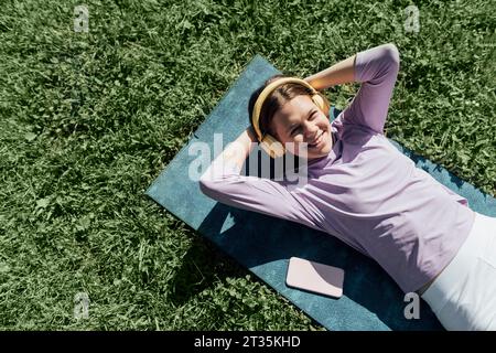 Ragazza adolescente sorridente che ascolta musica con le cuffie e che si esercita al parco Foto Stock