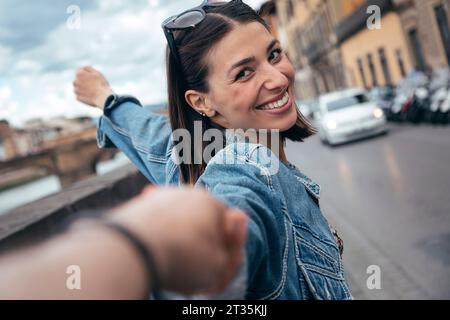 Donna sorridente che tiene la mano del partner per strada Foto Stock
