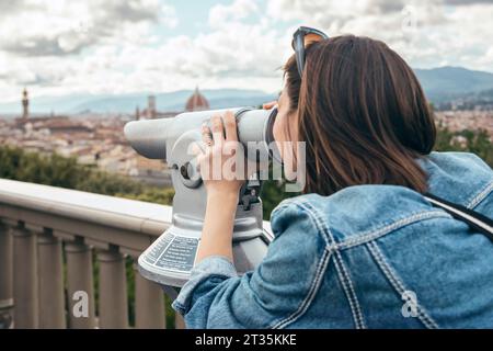 Donna che guarda attraverso il binocolo in piedi alla balaustra Foto Stock