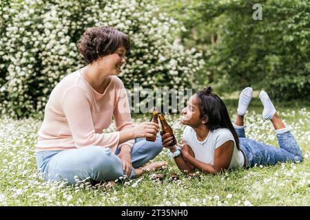 Donne sorridenti che tostano bottiglie di birra al parco Foto Stock