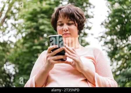 Giovane donna che usa lo smartphone al parco Foto Stock