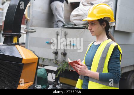 Serio operaio blu che scrive nel diario vicino al dumper Foto Stock