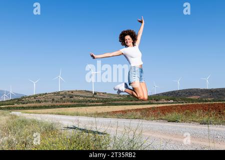 Donna allegra che salta davanti alle turbine eoliche Foto Stock