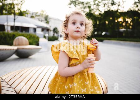 Ragazza contemplativa in abito giallo che regge la bacchetta a bolle d'aria Foto Stock