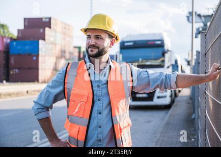 Un sorridente addetto alla logistica che indossa un elmetto in piedi davanti al camion Foto Stock