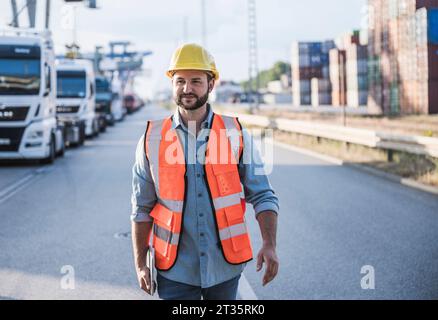 Sorridere il lavoratore della logistica che indossa elmetto e cammina con un tablet PC in viaggio Foto Stock