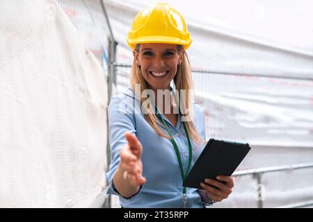 Ingegnere sorridente che fa una stretta di mano tenendo in mano un tablet PC Foto Stock