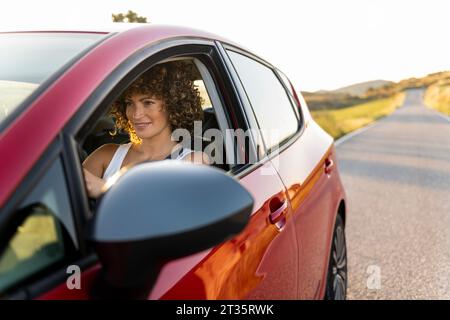 Donna sorridente che guida un'auto su strada Foto Stock